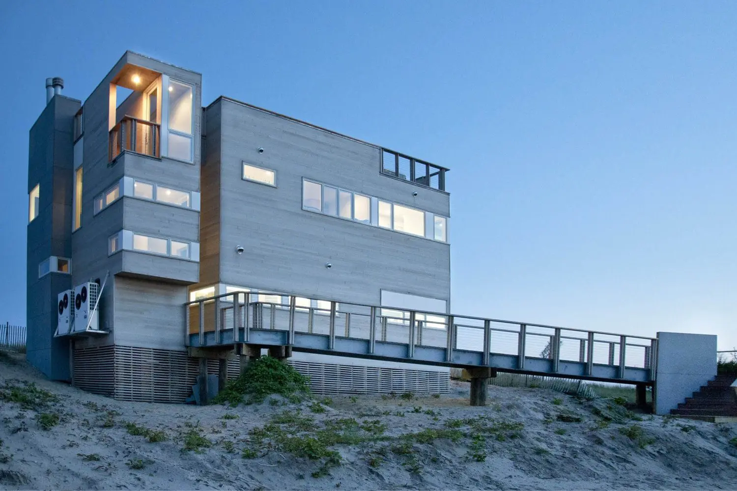 Modern beach house with large windows and a wooden boardwalk at sunset.