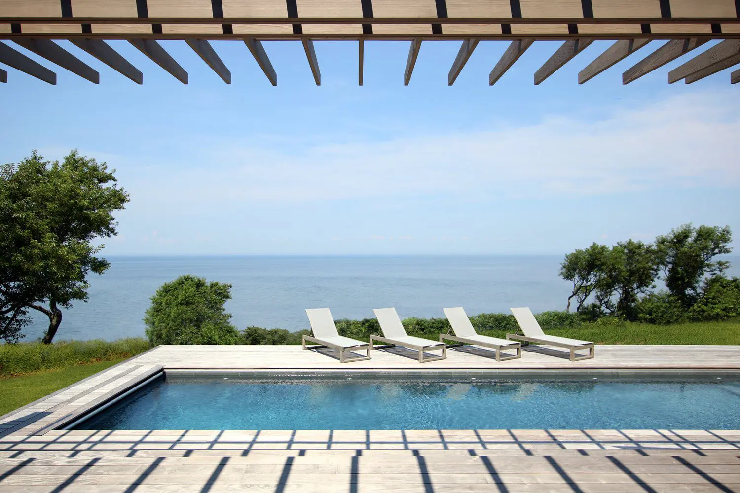 Luxurious poolside lounge chairs with ocean view under pergola.