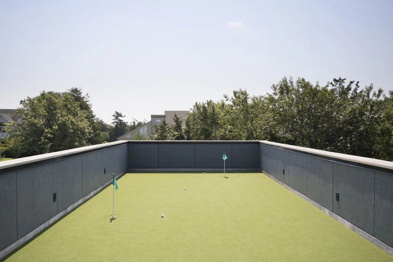 Empty rooftop terrace with green artificial grass and railing under clear sky.