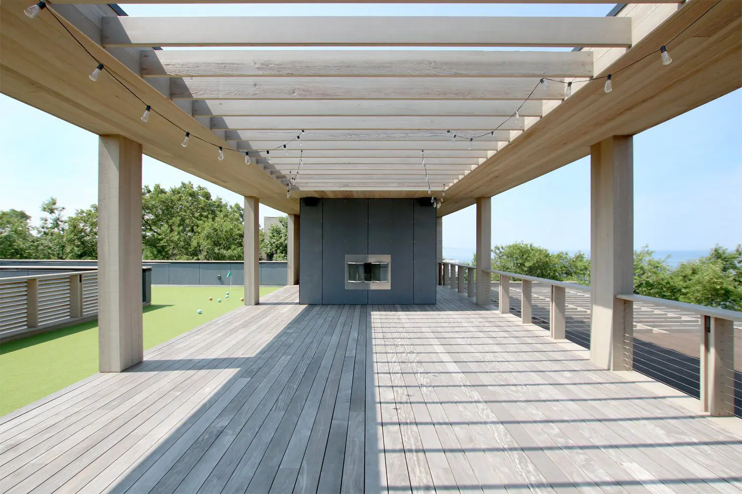 Empty wooden deck with pergola and fireplace on a sunny day.