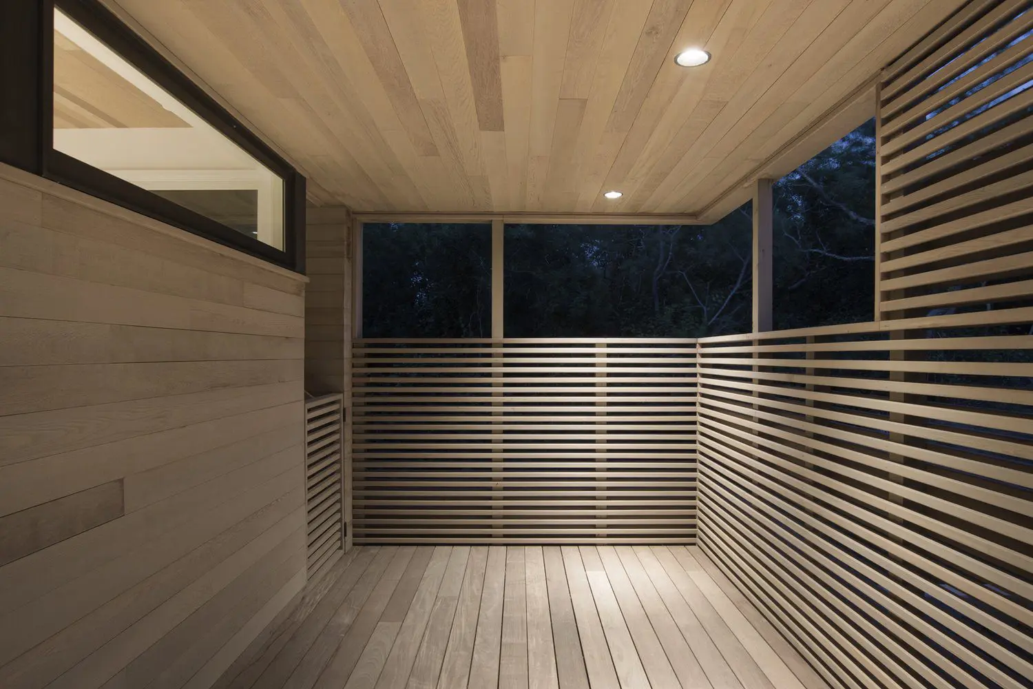 Modern wooden balcony with horizontal slats and recessed lights at night.