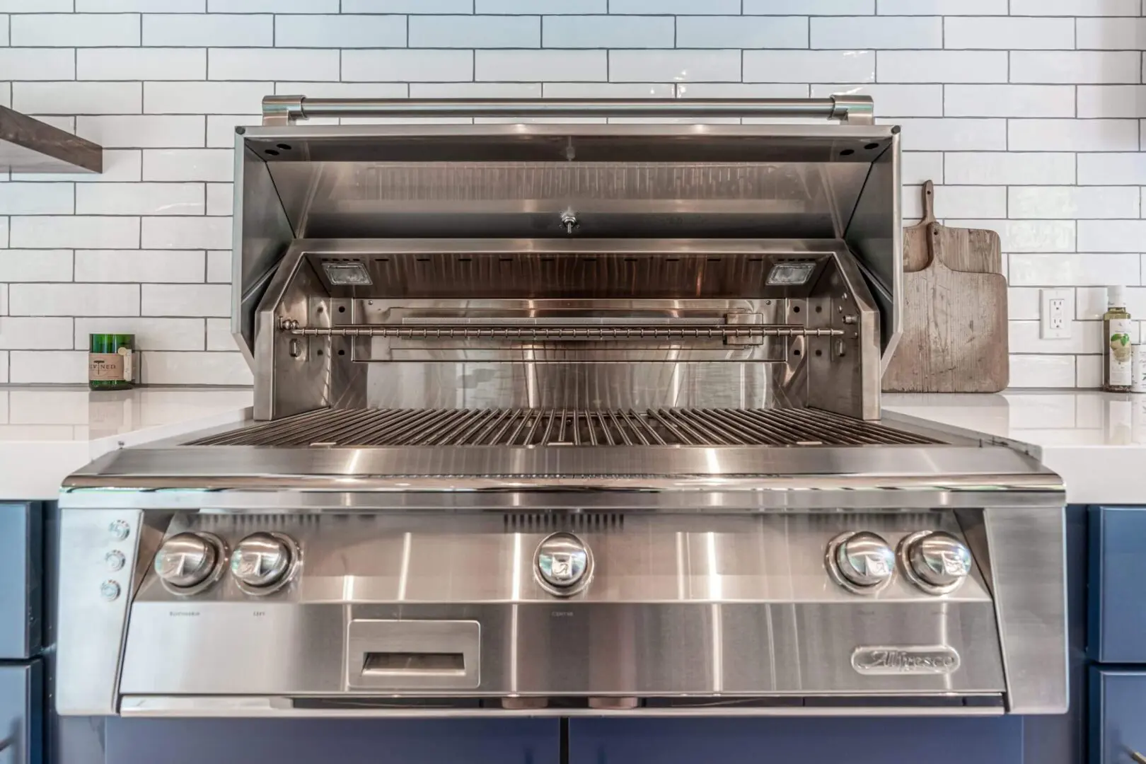 A modern stainless steel outdoor gas grill with open lid and control knobs.