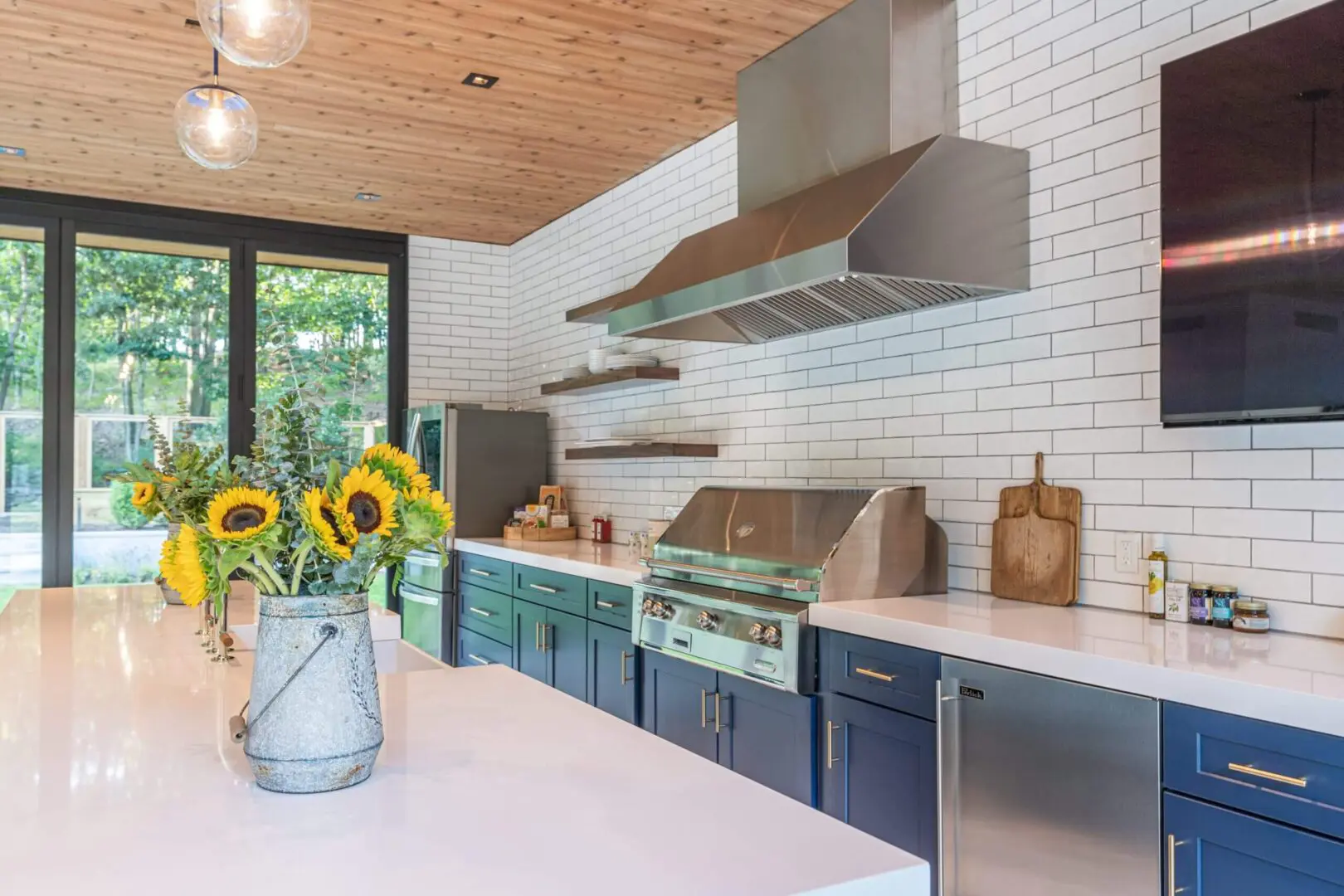 Modern kitchen with blue cabinets, stainless steel appliances, and sunflowers on the counter.