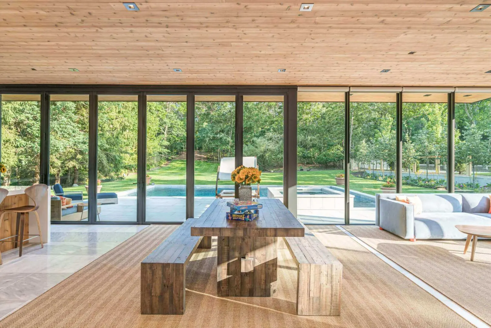 Modern dining area with wooden furniture and large glass doors overlooking a pool and garden.