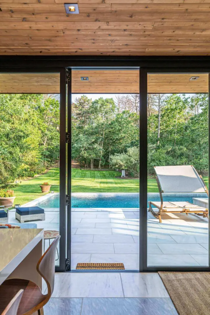 View of a serene backyard with a pool and lounge chairs through glass doors.