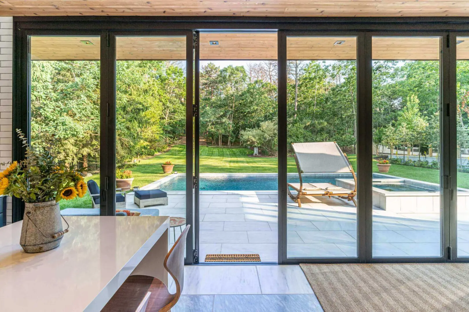 Sunlit patio with pool and lounge chairs seen through sliding glass doors.