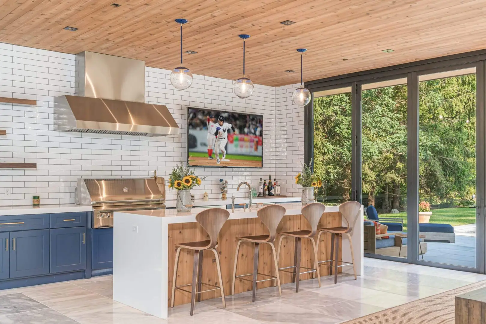 Modern kitchen with wooden stools and large windows overlooking greenery.