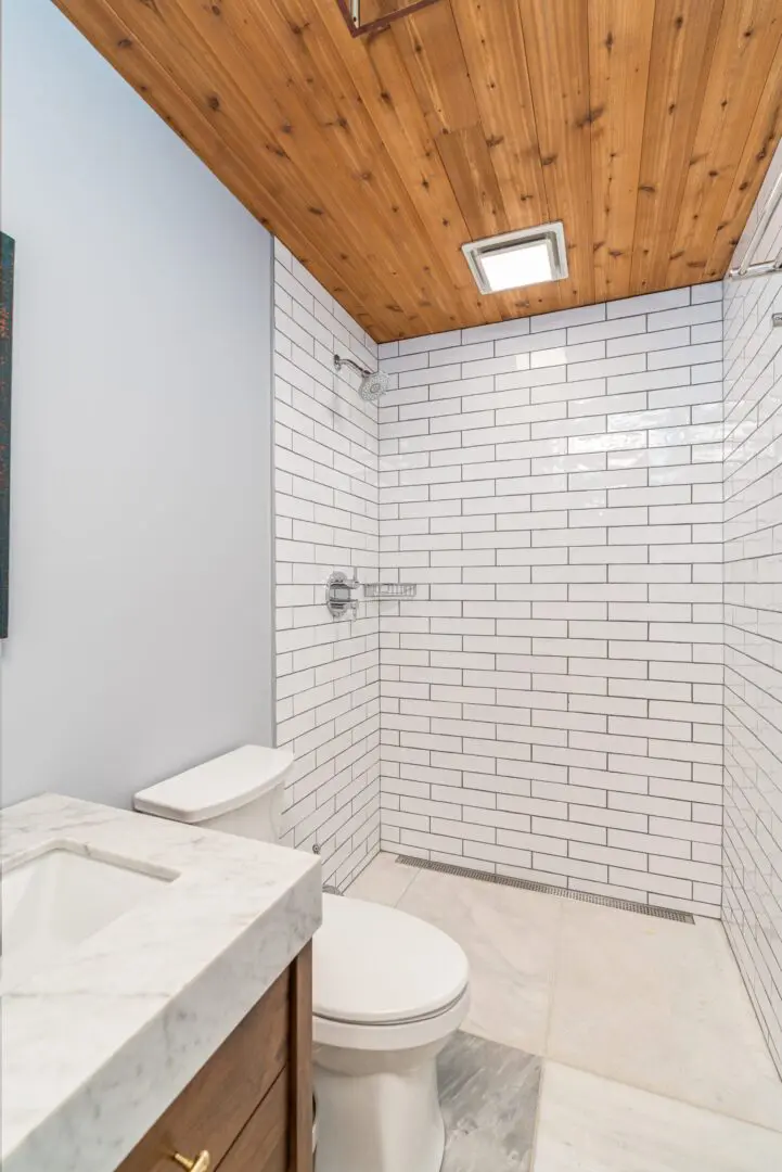Minimalist bathroom with white subway tile shower and wooden ceiling.