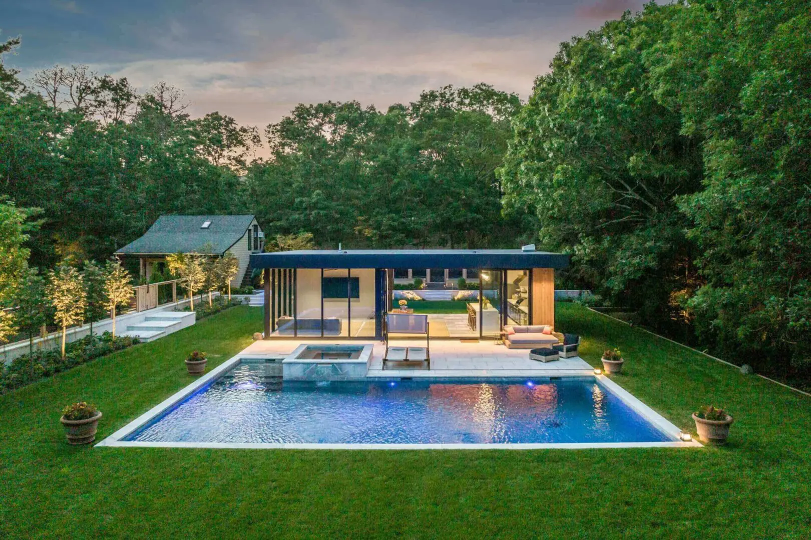 Modern house with a sleek pool at sunset, surrounded by greenery.