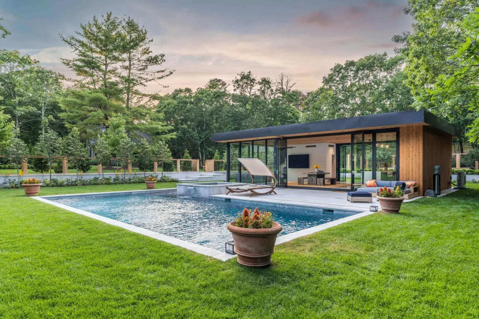 A modern house with a pool surrounded by greenery at sunset.