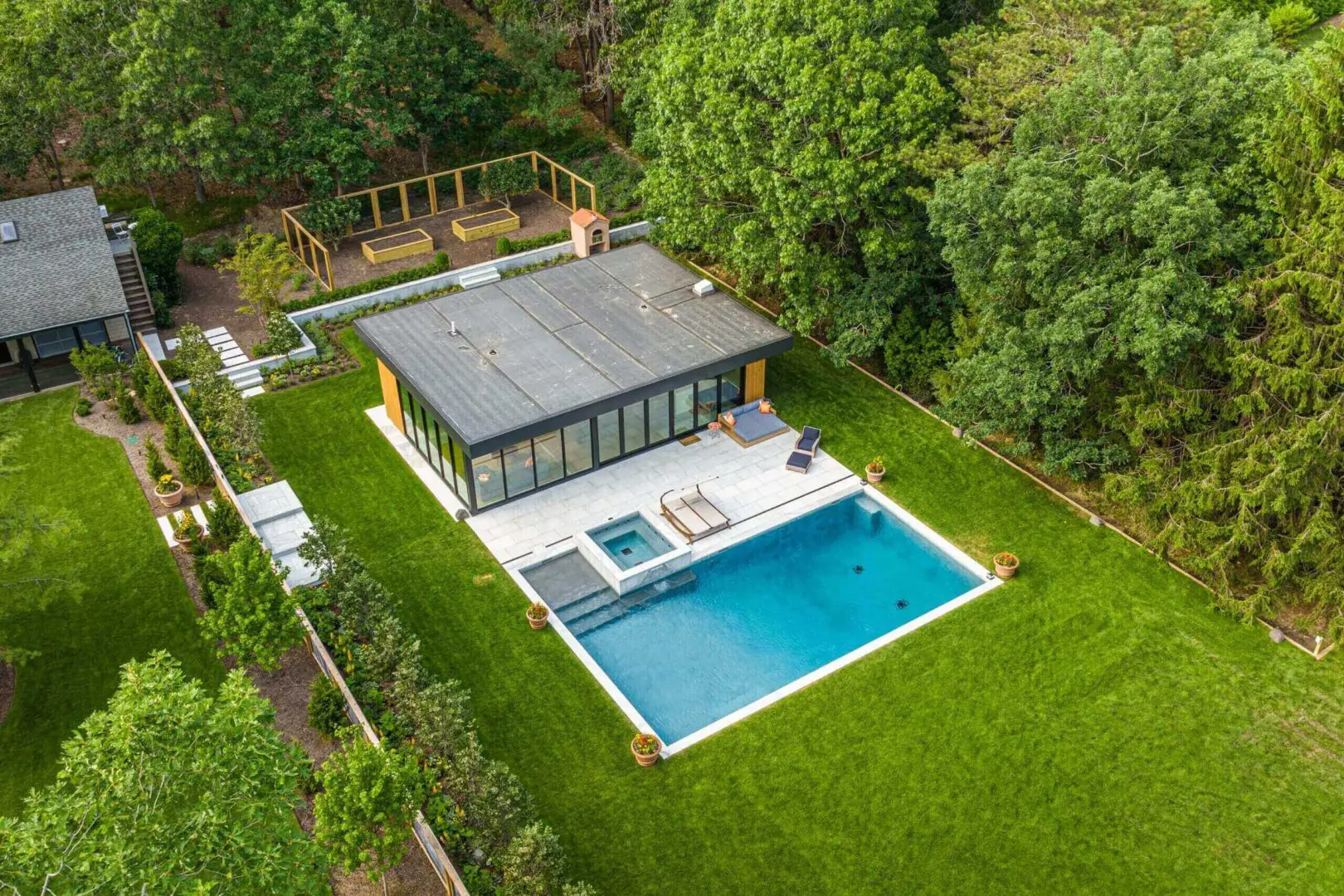 Modern house with a pool and sunbathing area in a lush green garden.