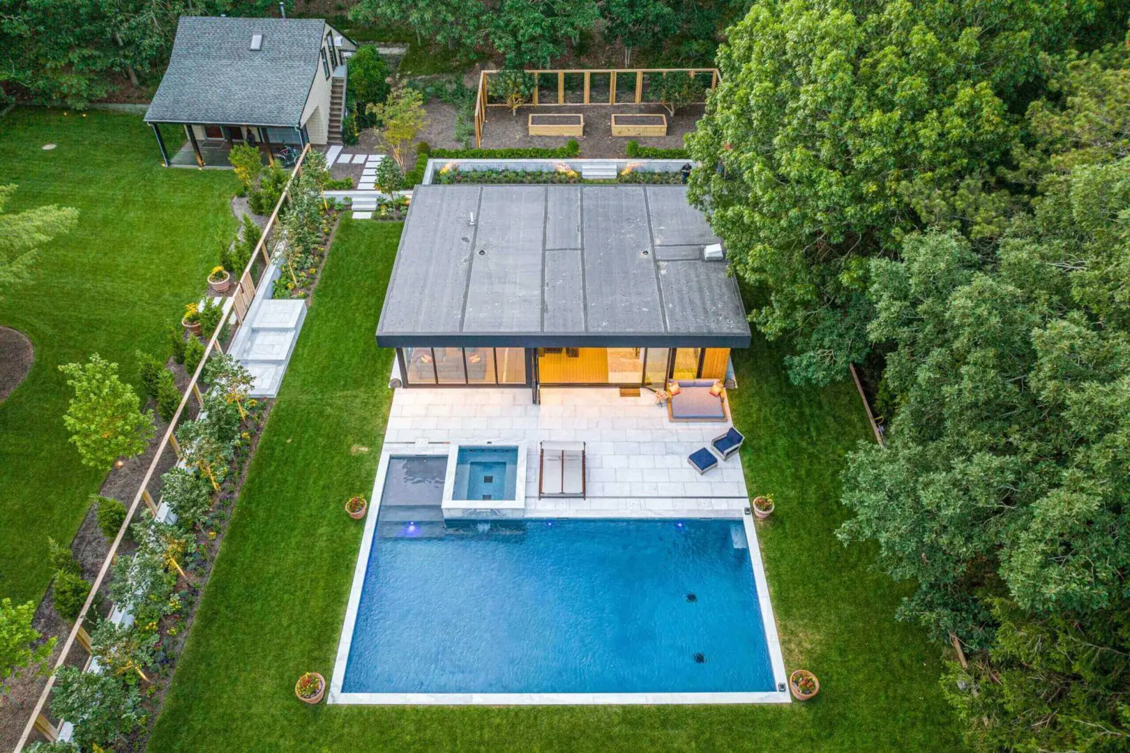 Modern house with a large pool and hot tub in a green backyard.