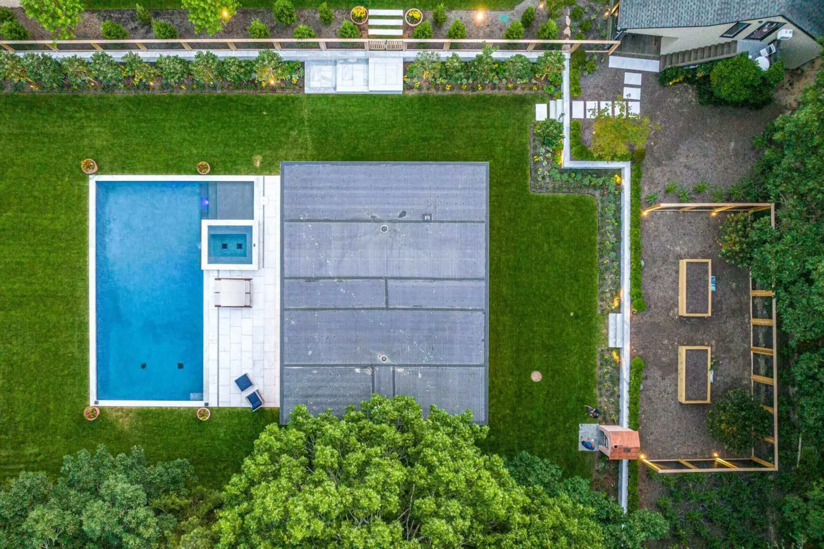 Aerial view of a modern backyard with a pool, patio, and green lawn.