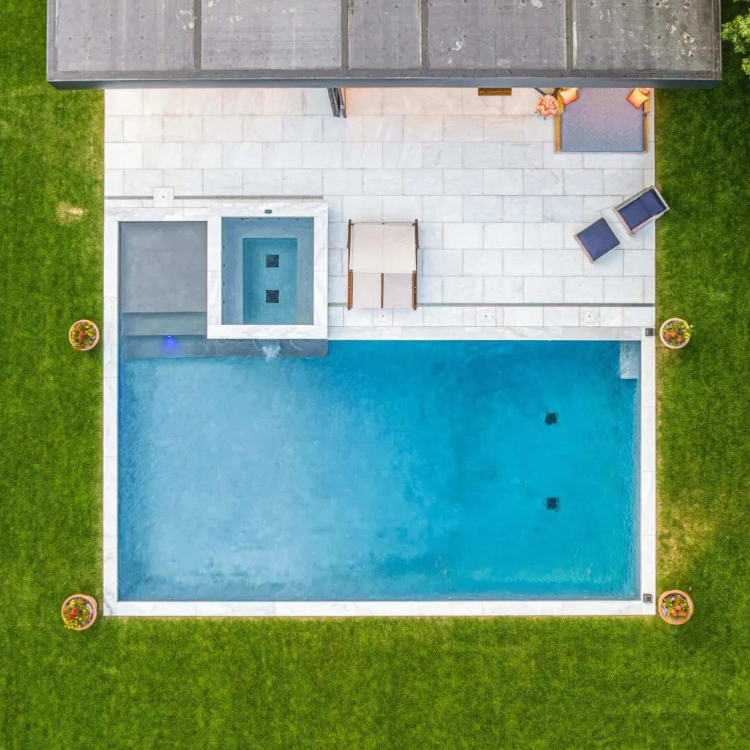 Aerial view of a modern rectangular pool with a jacuzzi and lounge chairs.