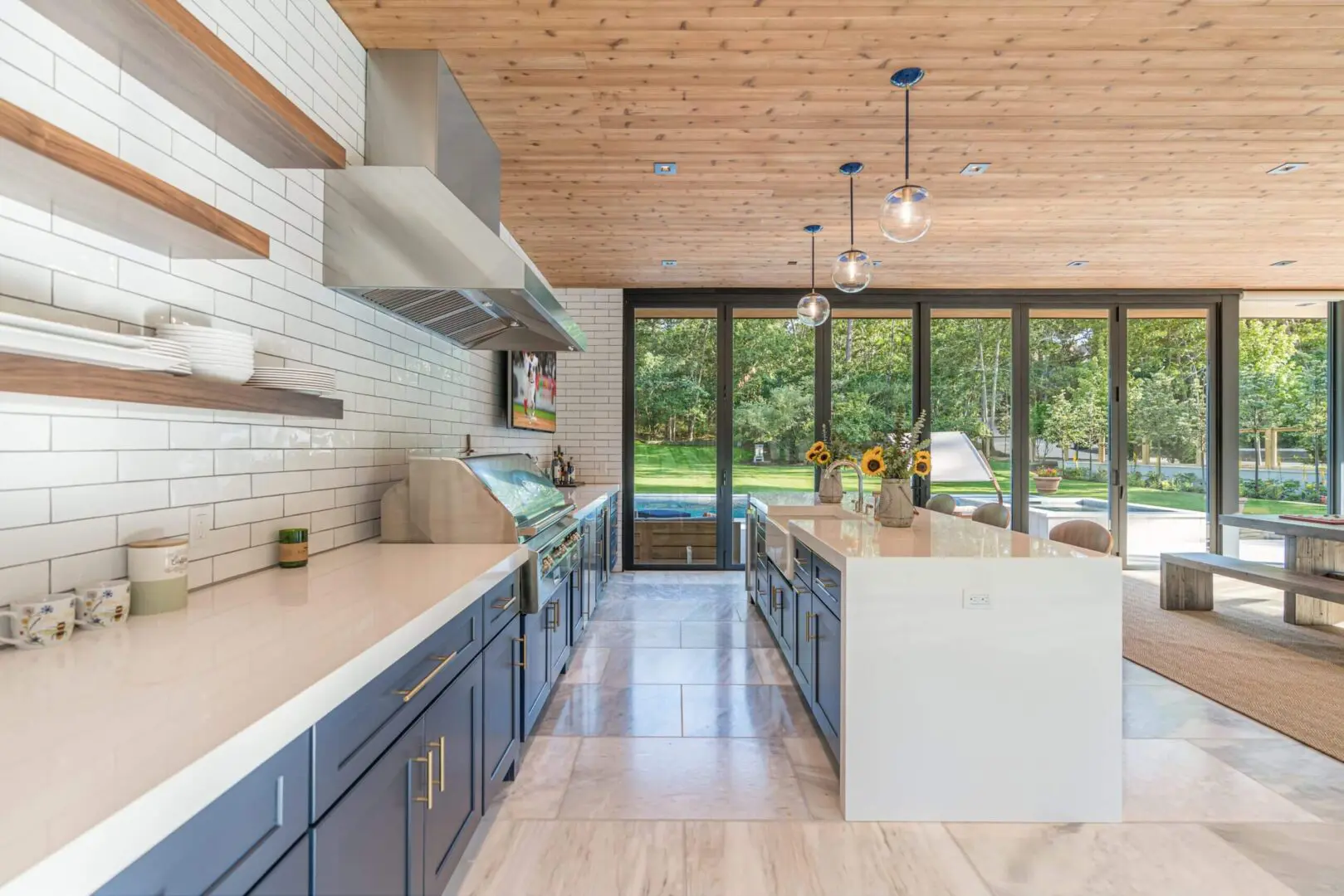 Modern kitchen with blue cabinets, white countertops, and large glass doors showing a garden.