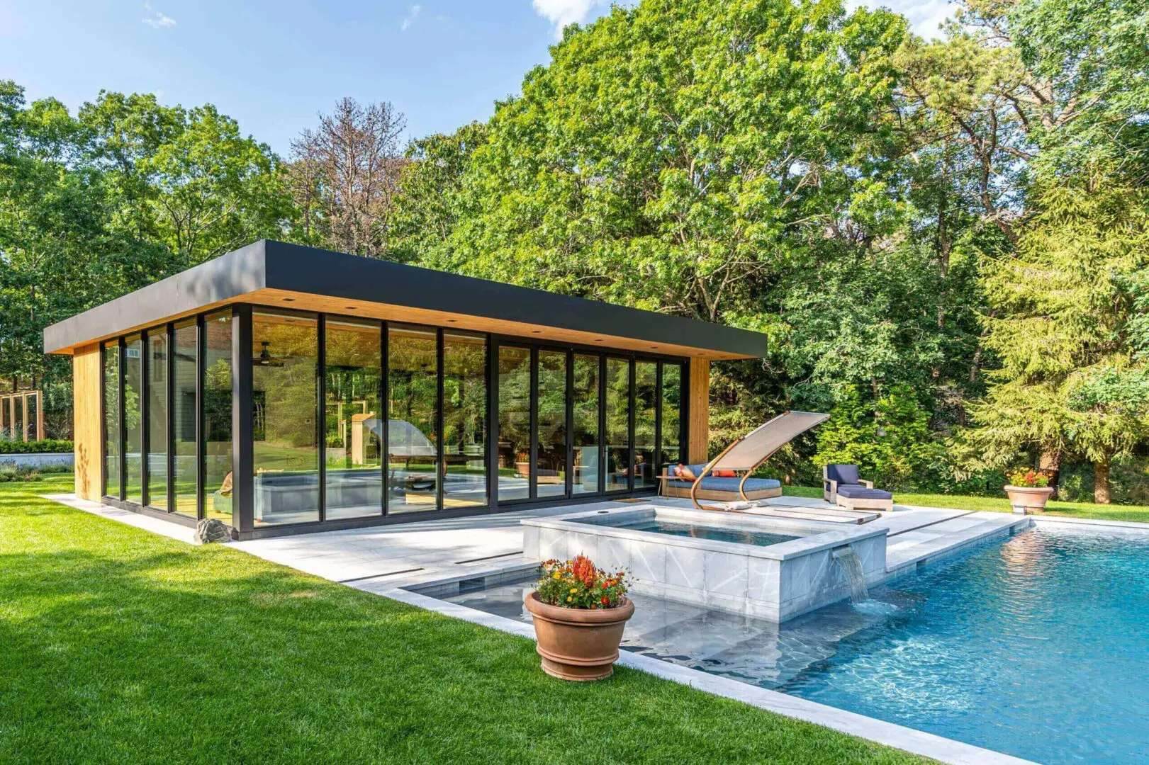 Modern pool house with glass walls next to a swimming pool.