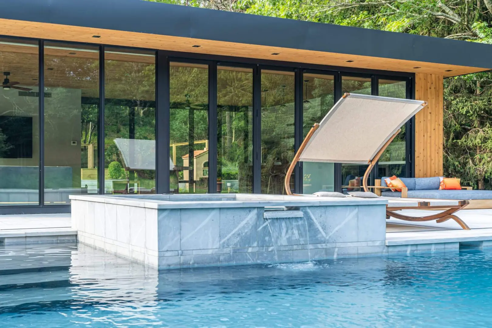 Modern pool with glass walls and lounge chairs beside it.