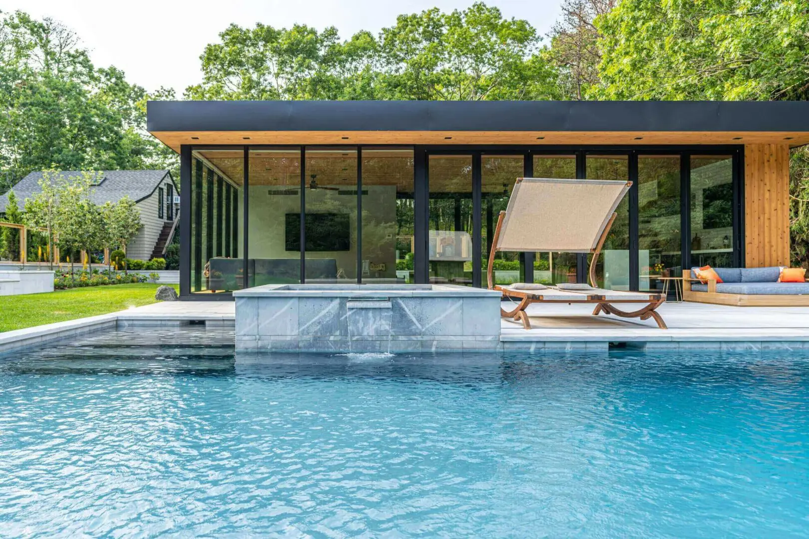 Modern pool with waterfall feature and lounge chairs beside it.