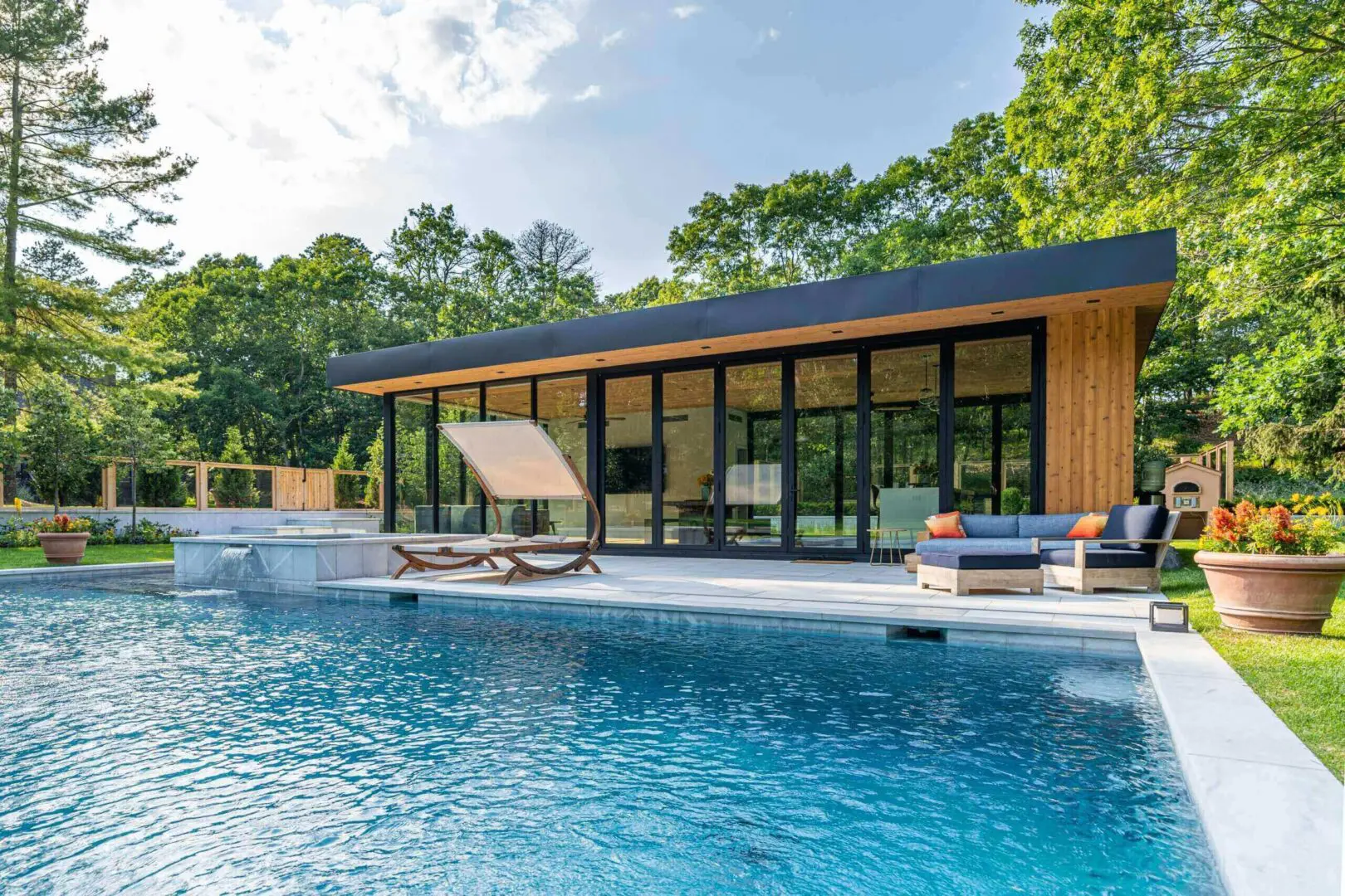 Modern house with large glass windows beside a serene pool under a partly cloudy sky.