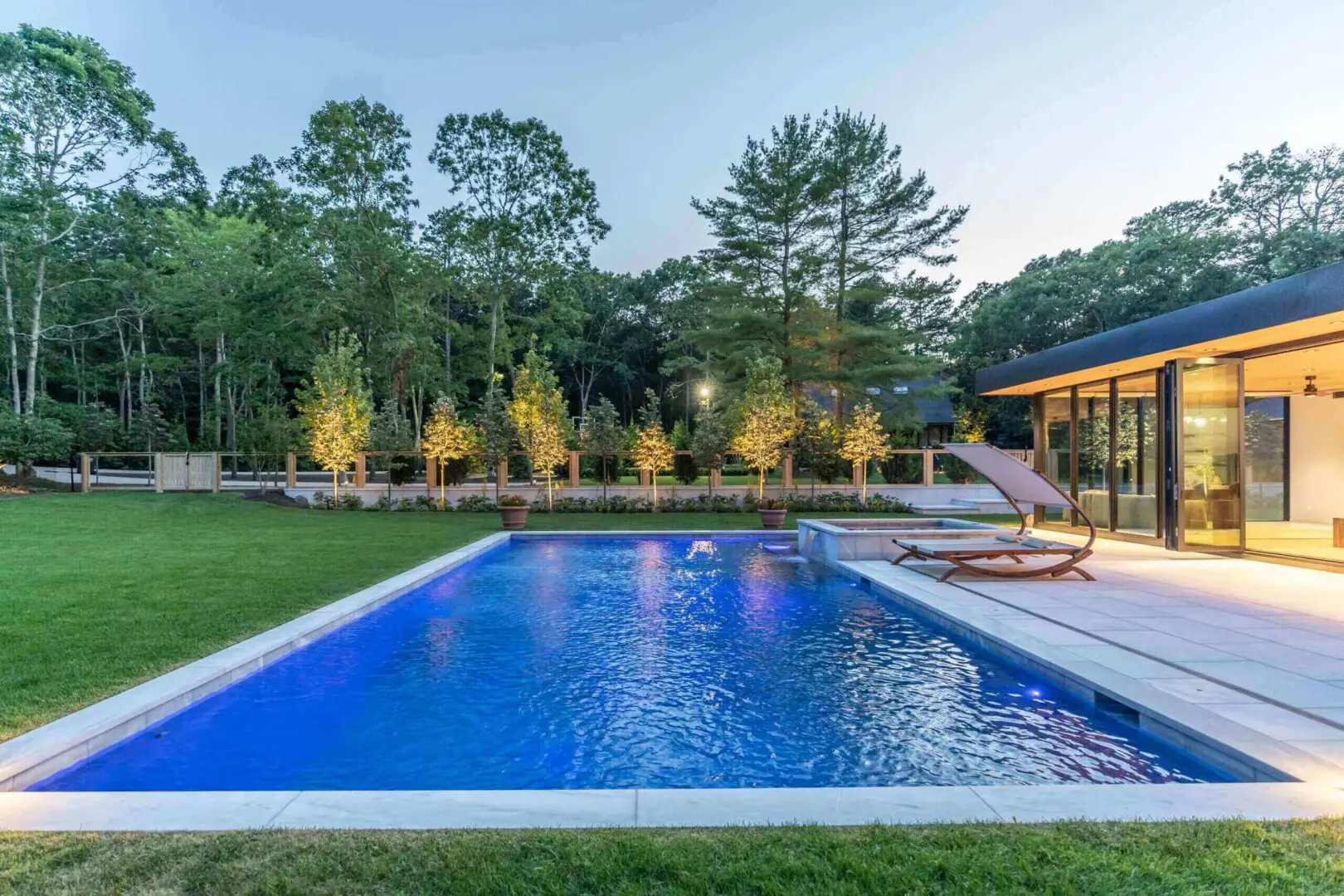 A serene outdoor pool with surrounding trees and seating area at dusk.