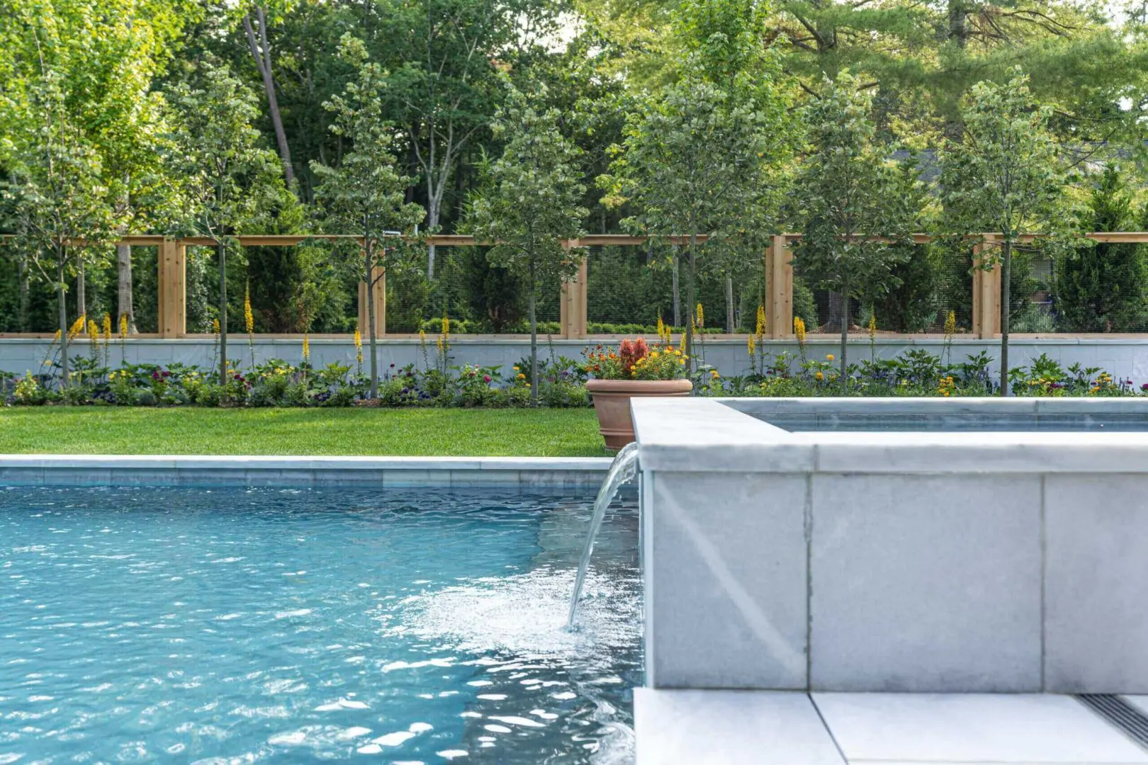 Water flowing from a modern pool fountain into a clear swimming pool.