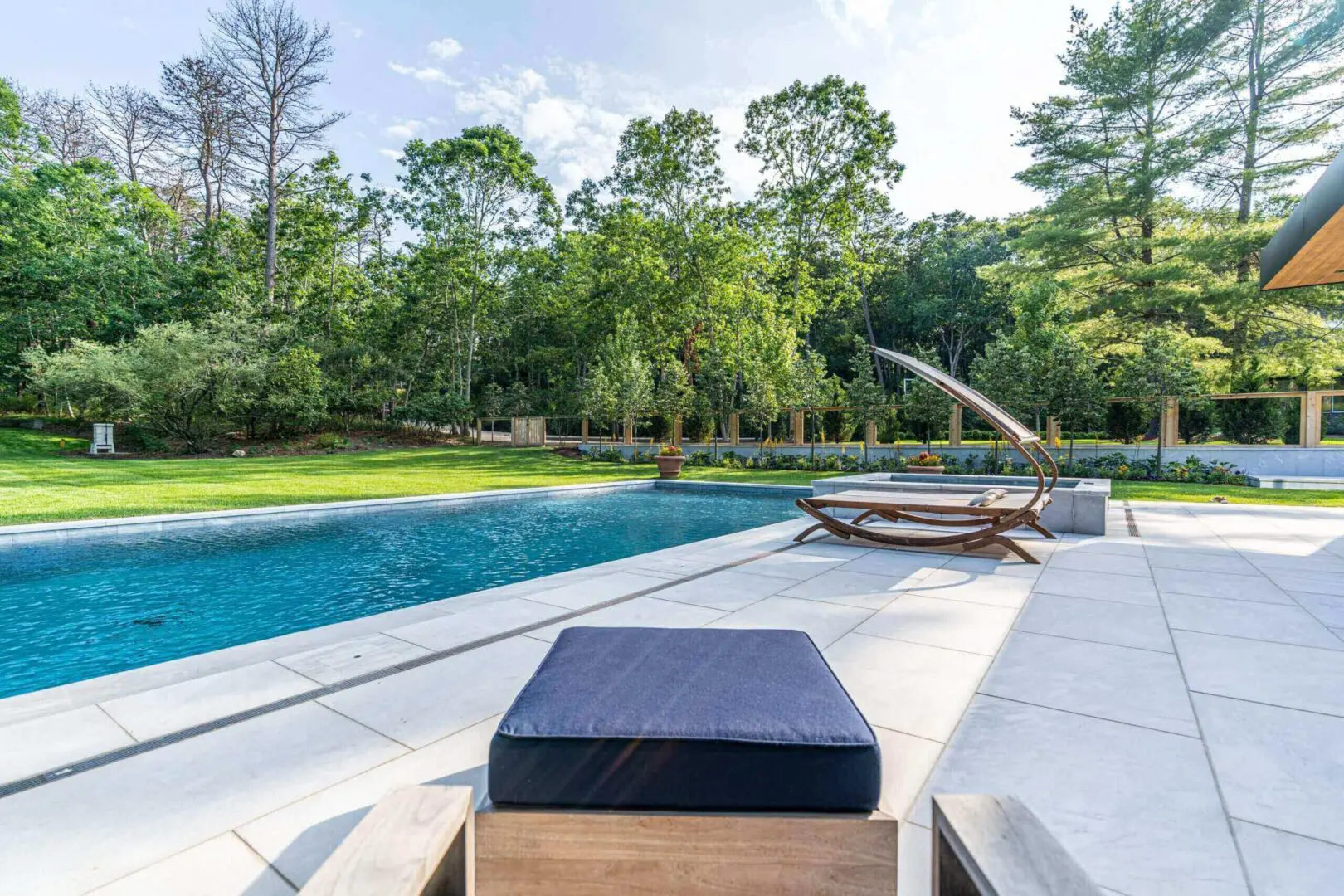 Modern outdoor pool area with lounge seating and trees.