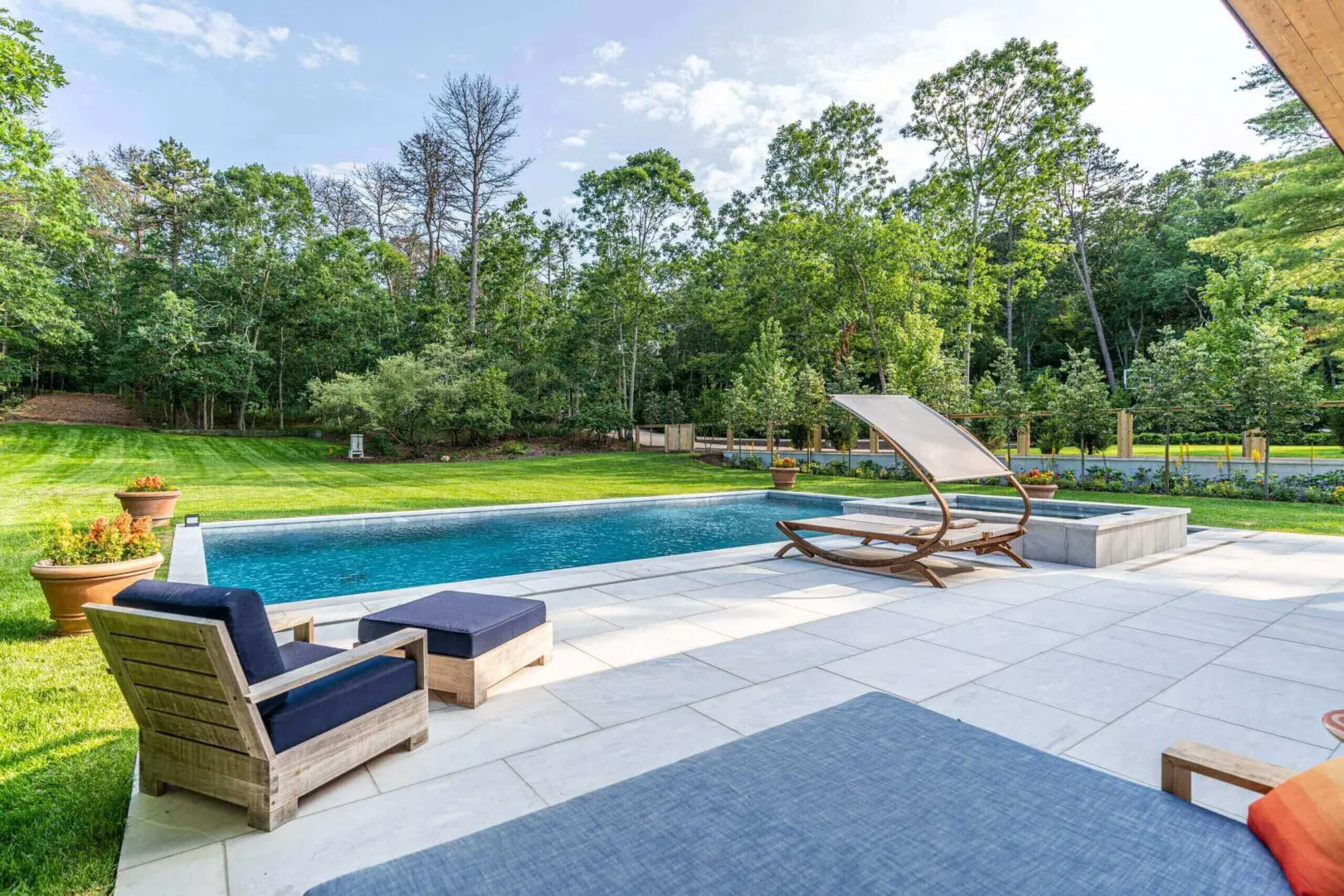 Modern outdoor pool area with lounge chairs and a wooden table under a large umbrella.