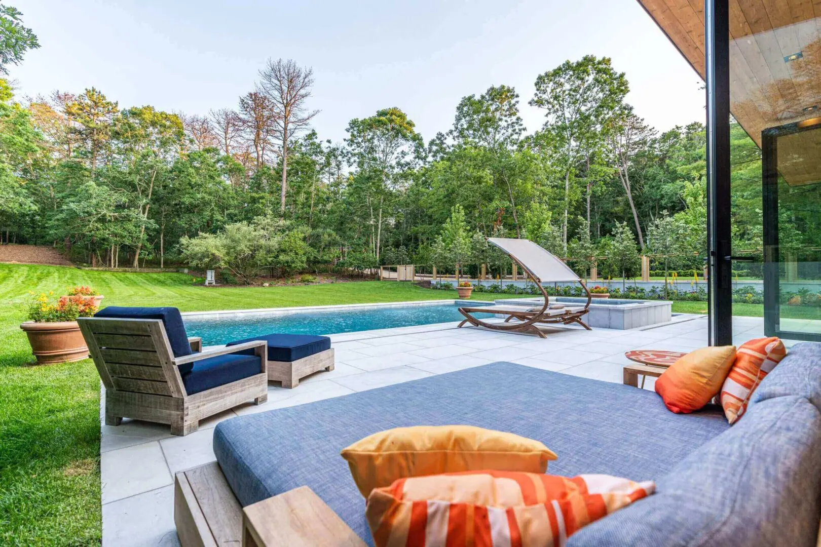 Modern backyard patio with seating, pool, and greenery.
