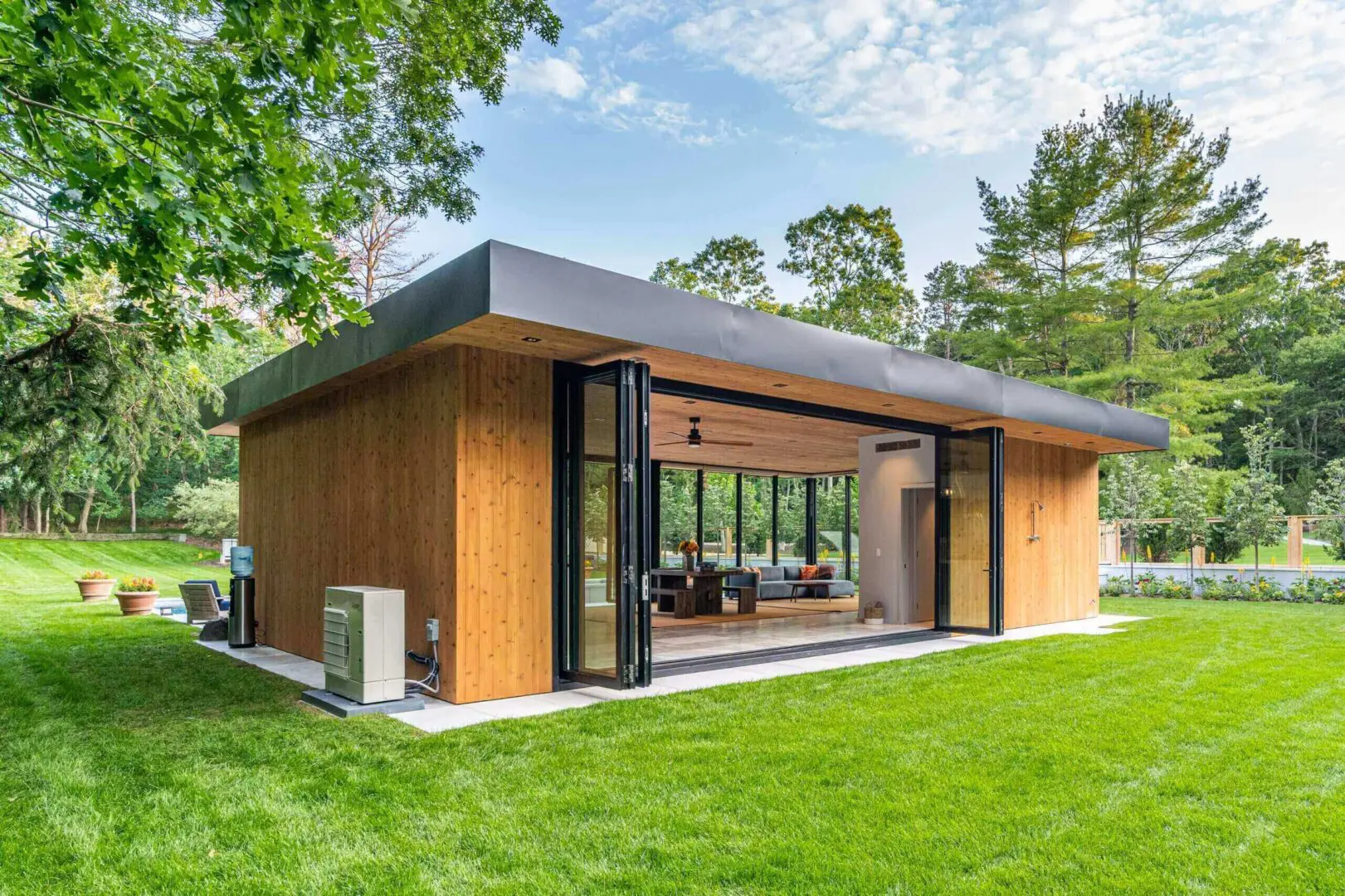 Modern wooden house with large glass doors in a green yard.