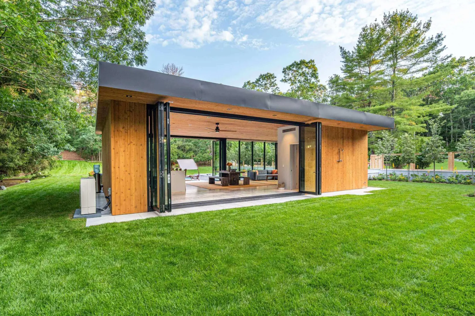 Modern wooden house with large glass windows and a lush green lawn.