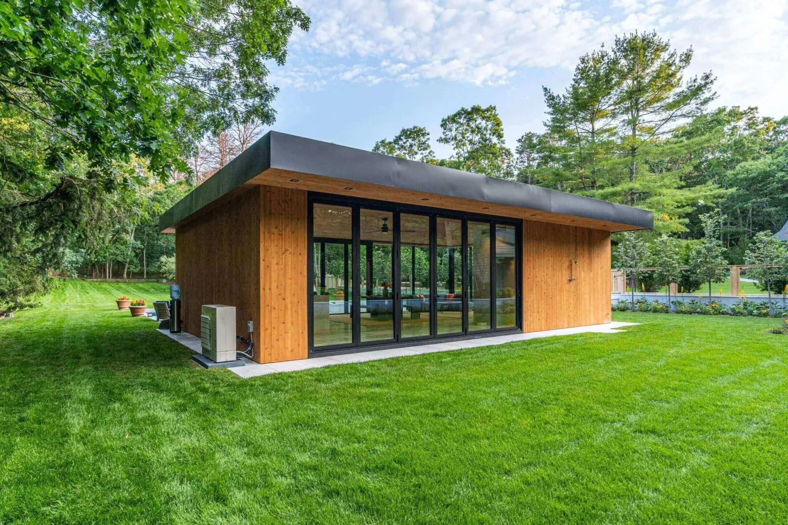 Modern wooden house with large glass windows in lush green surroundings.