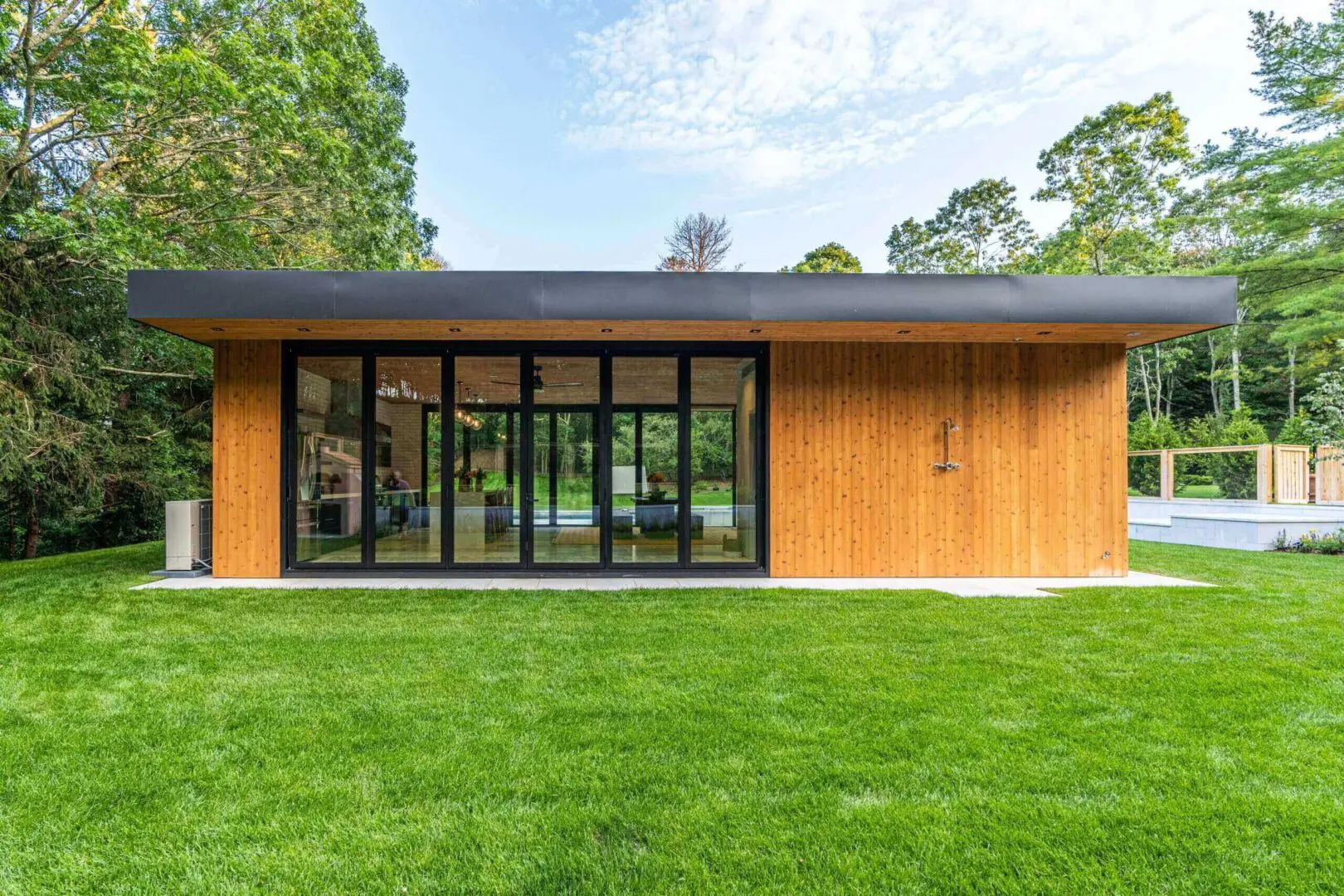 Modern wooden house with large glass doors and a lush green lawn.