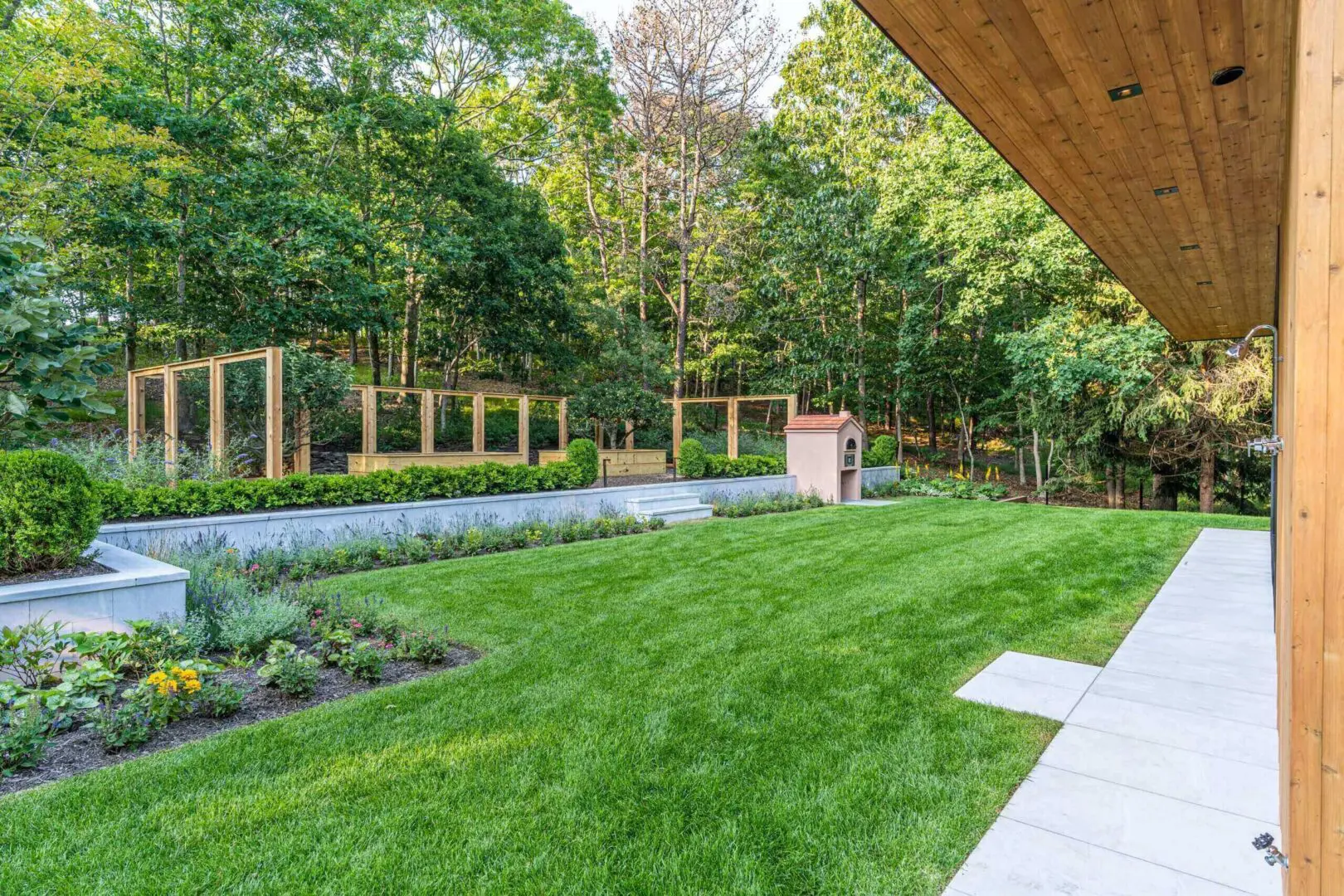 A lush backyard with green grass and a garden area under a wooden roof.