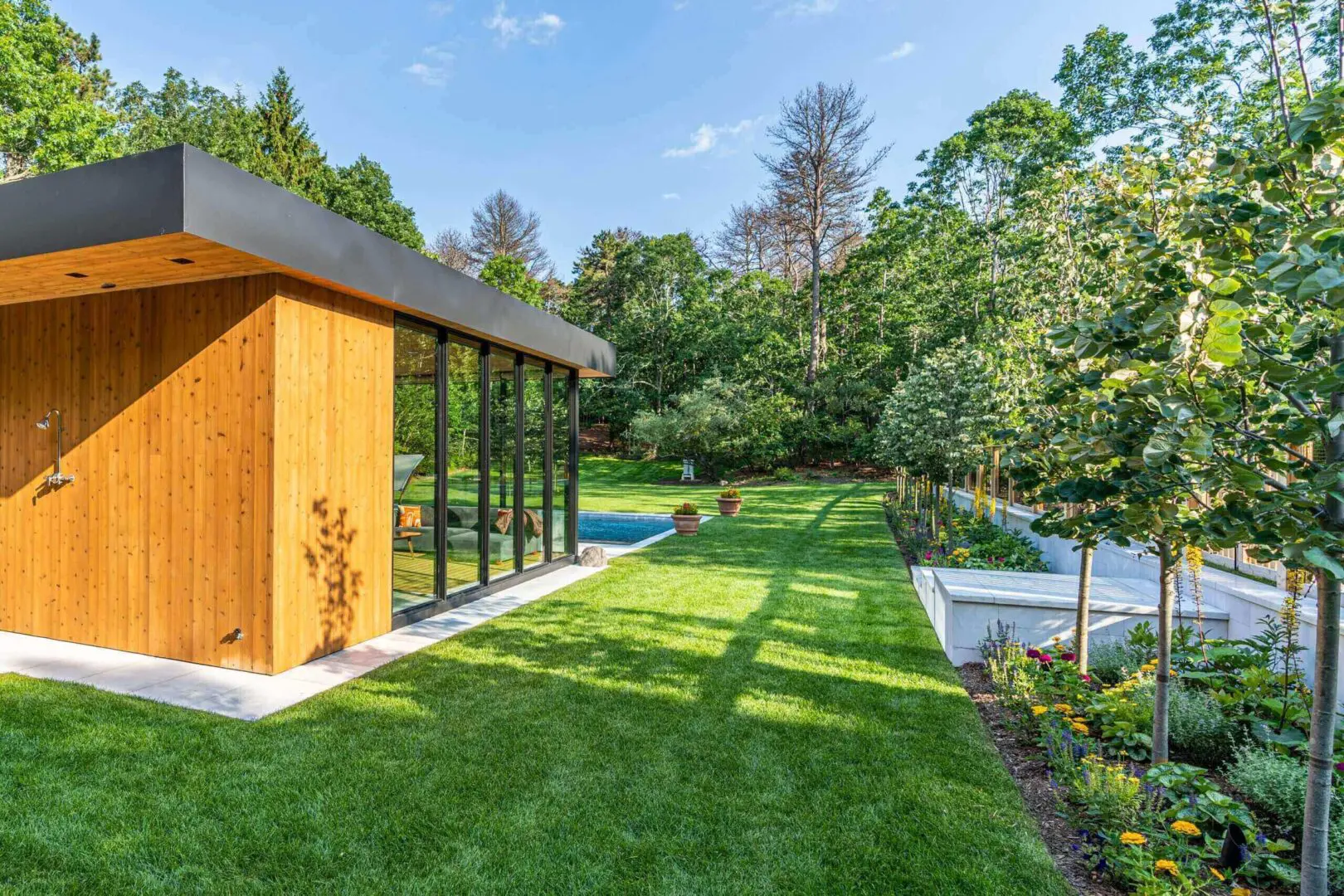 Modern garden house with glass walls overlooking a green lawn and pool.