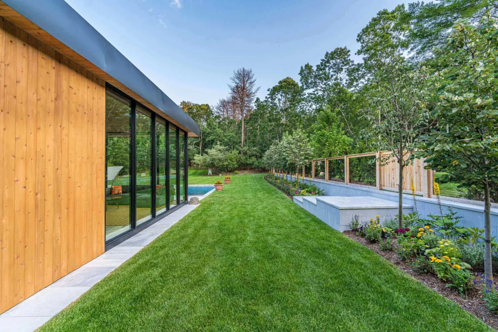 Modern house with large windows and a lush green lawn beside a swimming pool.