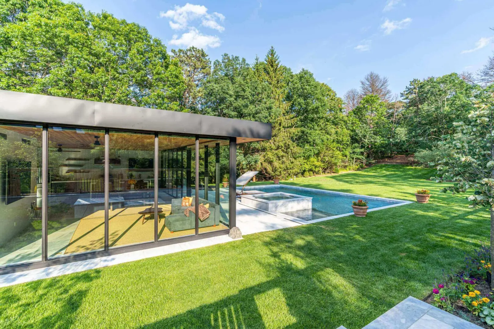 Modern backyard with a pool and glass-walled patio surrounded by greenery.