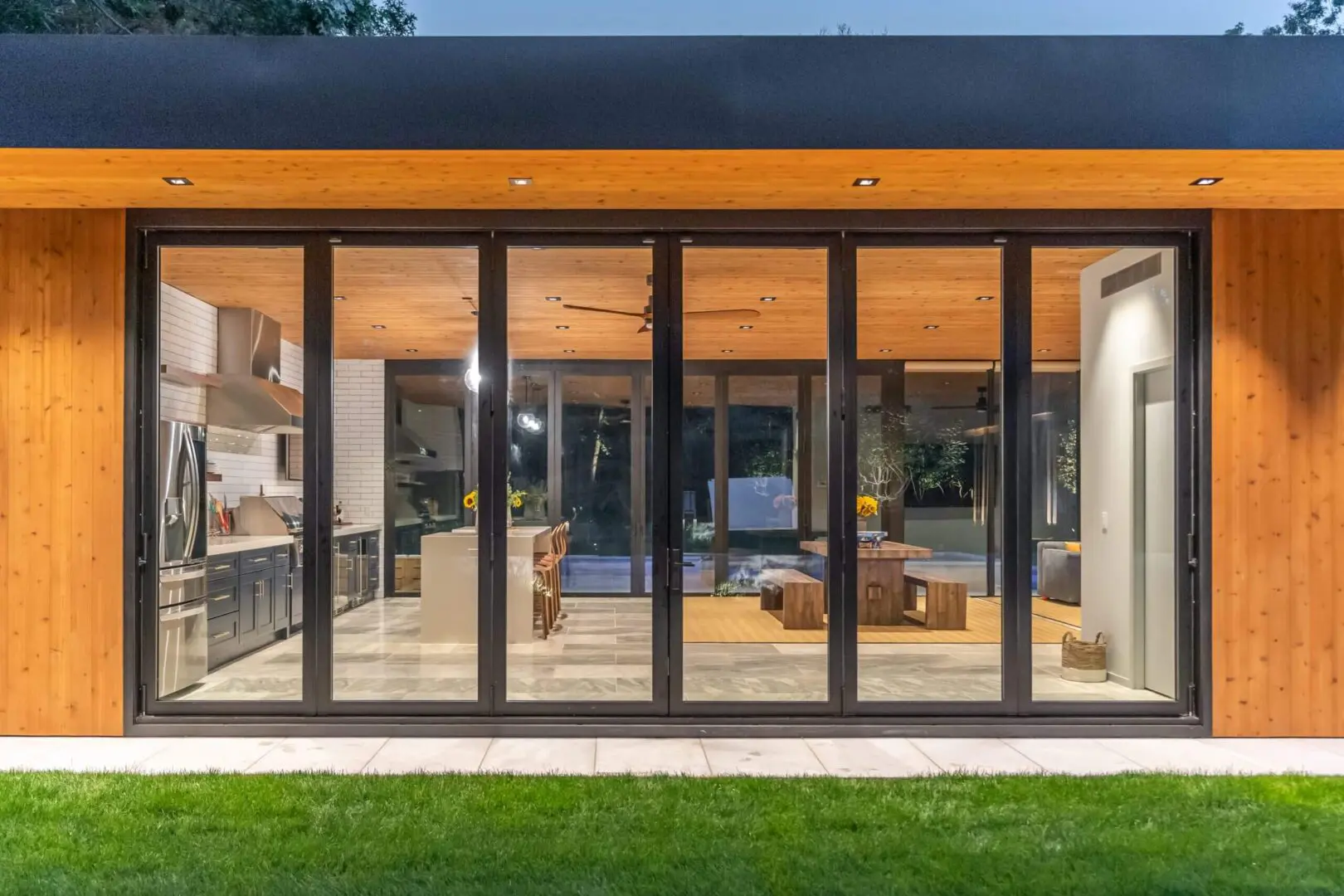 Modern house exterior with large glass doors opening to a cozy living room.