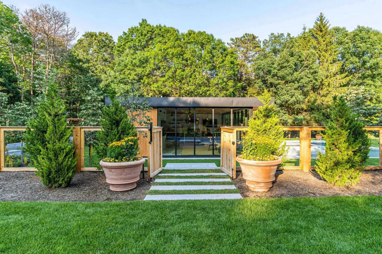 Modern outdoor pavilion with wooden roof and large planters in lush garden.