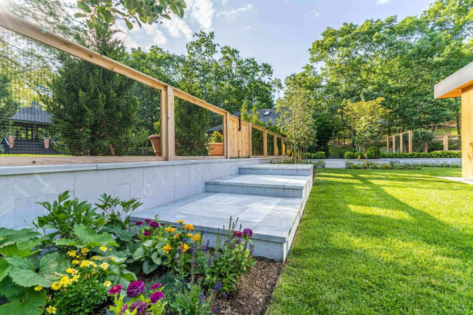 A modern outdoor patio with concrete steps and a wooden railing overlooking a lush green garden.
