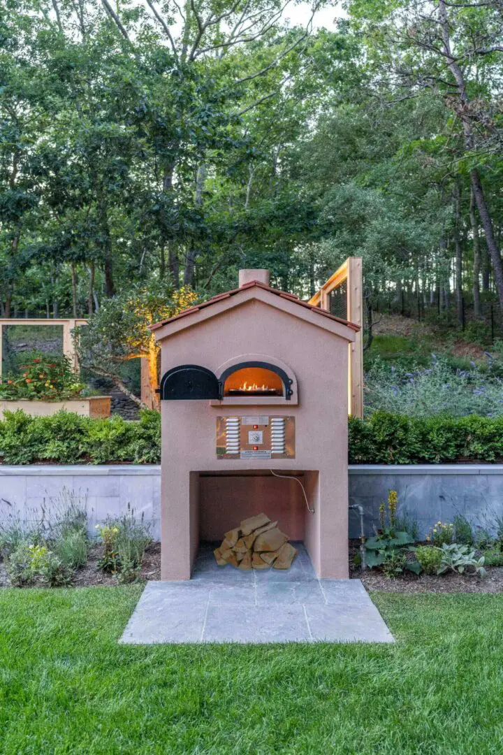 Outdoor brick pizza oven with fire inside in a garden setting.