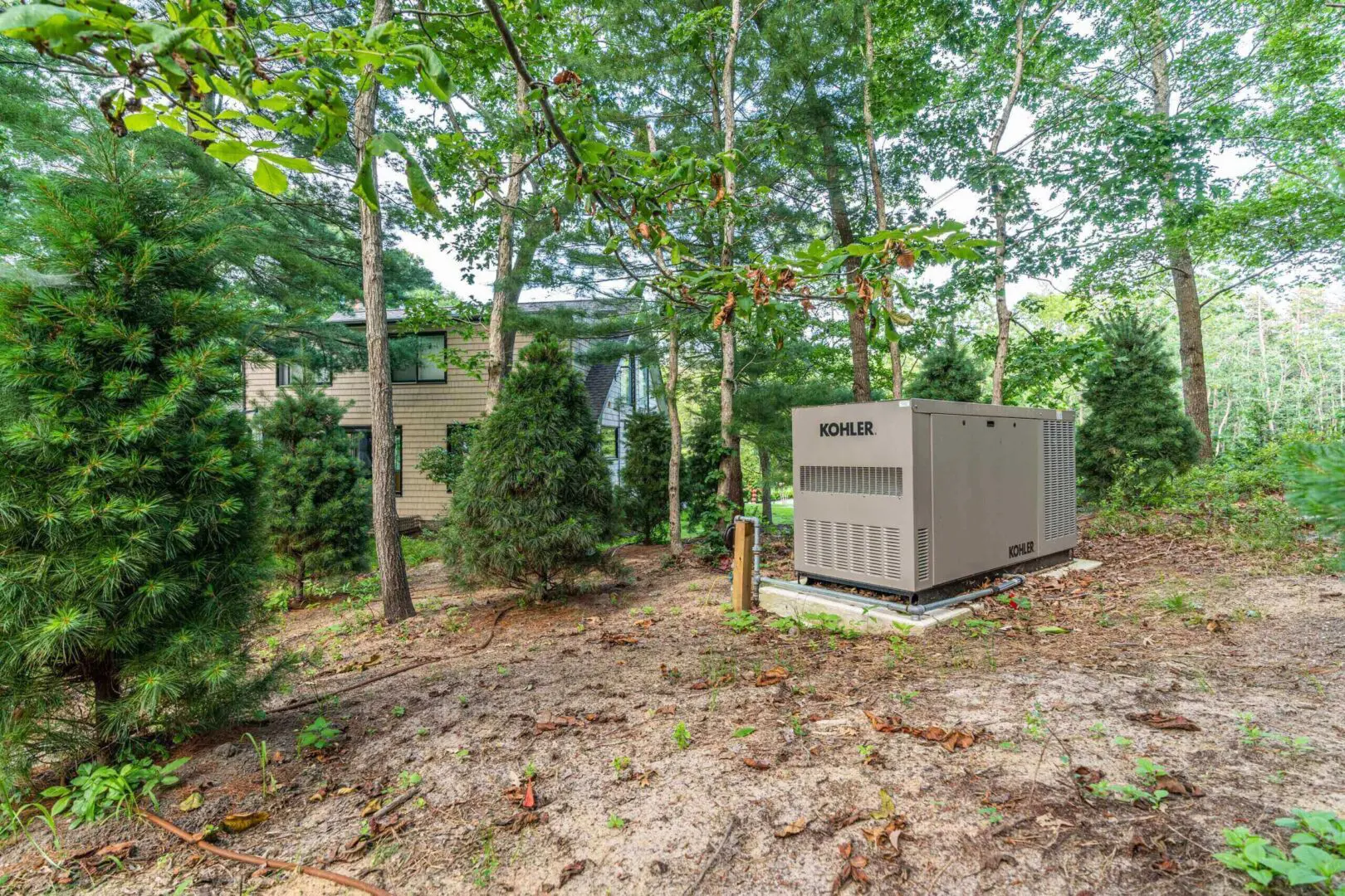 A large outdoor generator set among trees near a building.