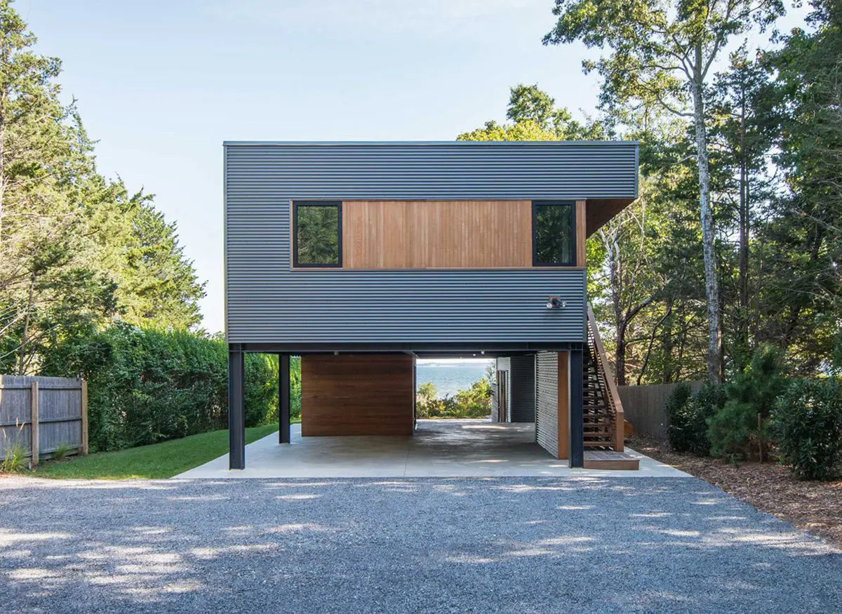 Modern elevated house with sleek metal and wood exterior.