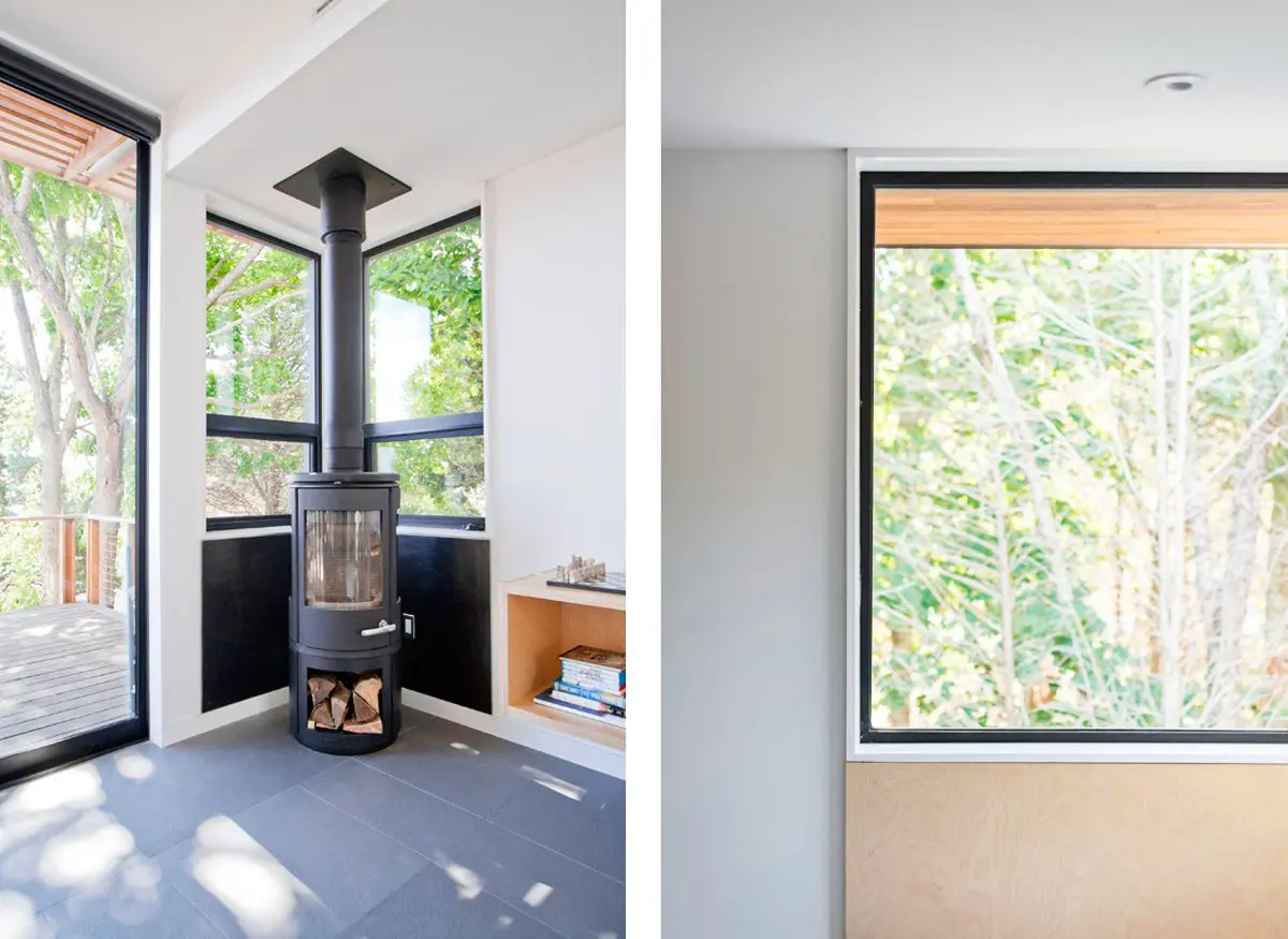 A modern wood stove in a corner by large windows with a scenic outdoor view.