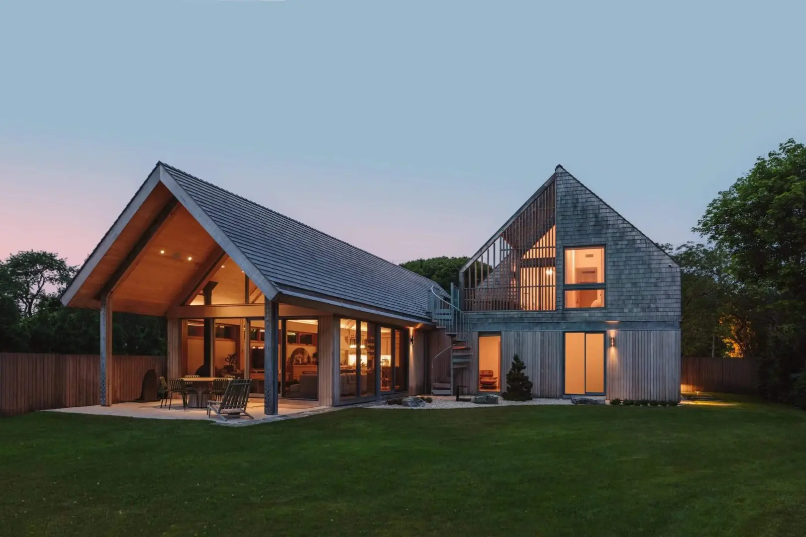 Modern house with large windows and warm lighting at dusk.