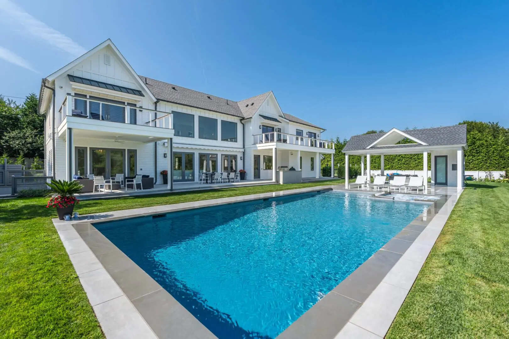 Luxurious modern house with a large swimming pool under clear blue sky.