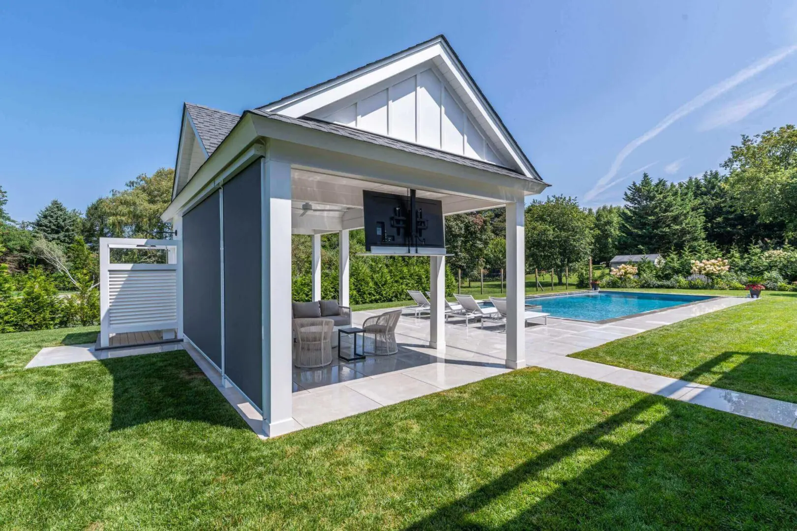Modern poolside cabana with seating and a grill under a blue sky.