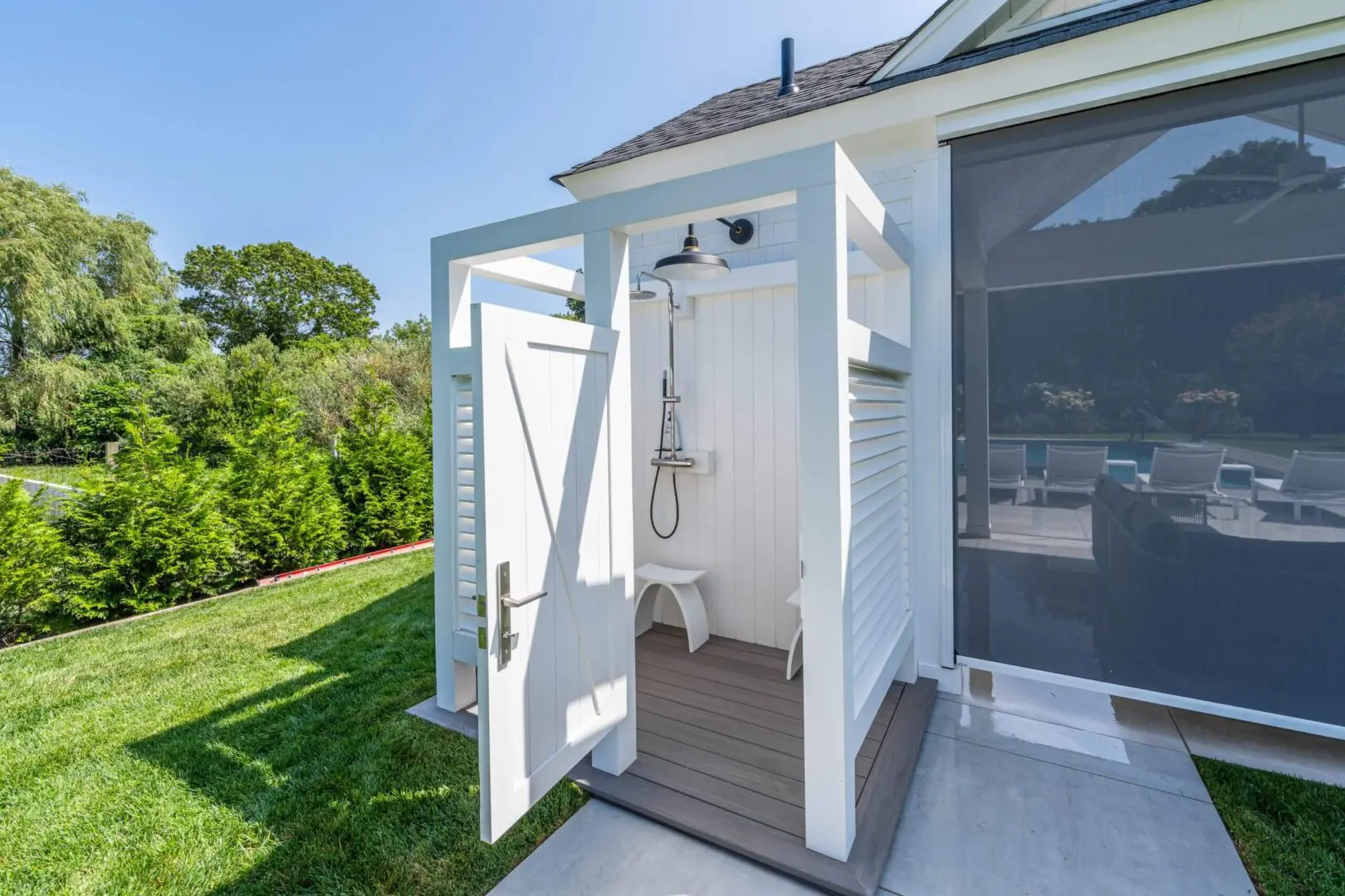 Outdoor shower attached to a house with white walls and wooden floor.