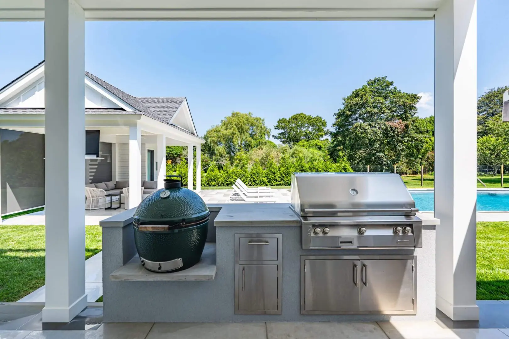 Modern outdoor kitchen with grill and smoker under clear sky.