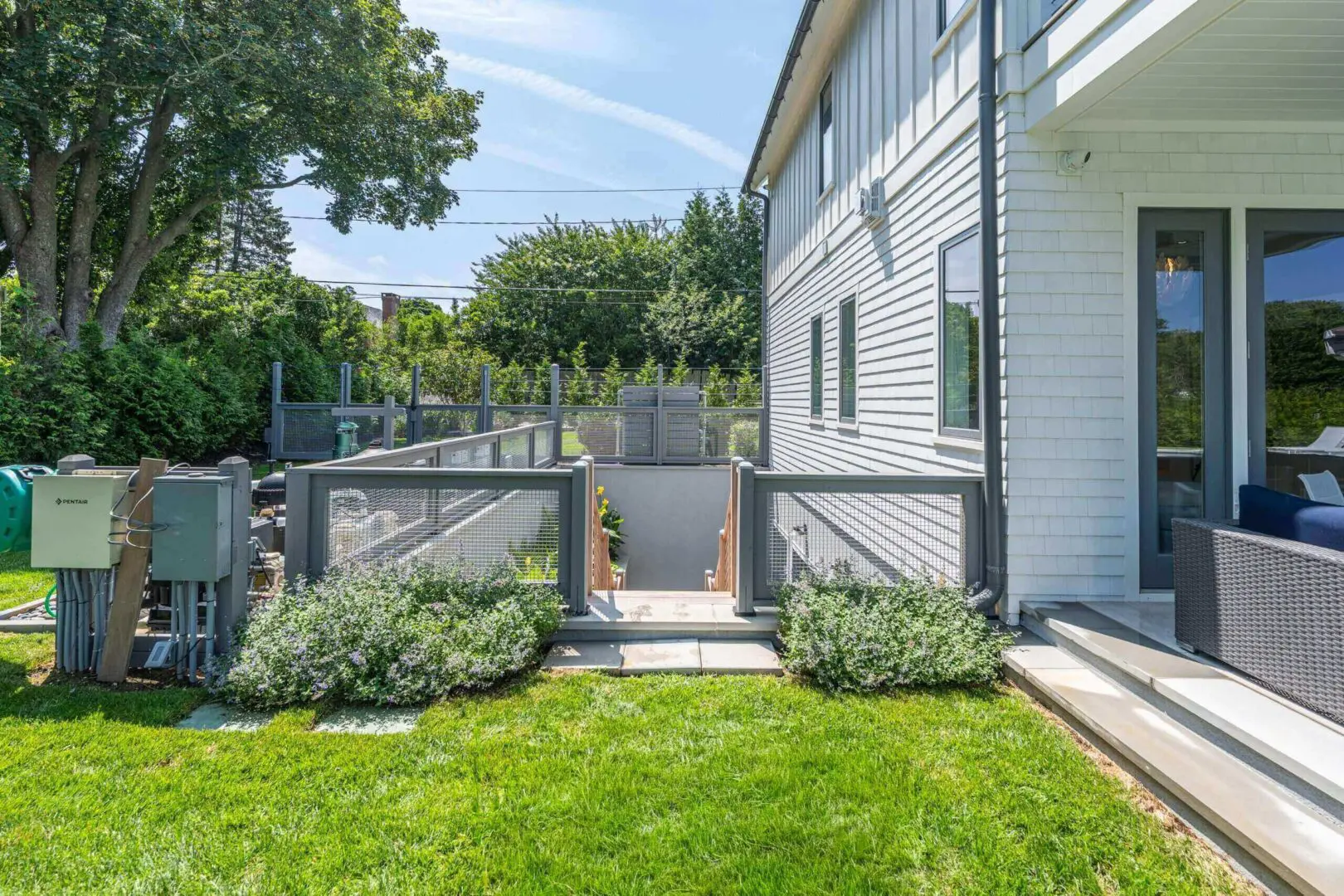Modern backyard with green lawn, plants, and white house exterior.