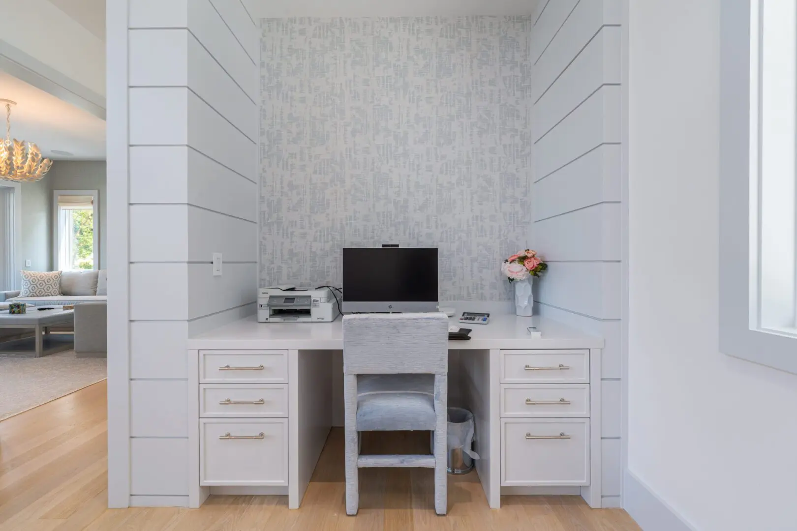 A minimalist workspace with a desk, chair, and computer in a bright room.
